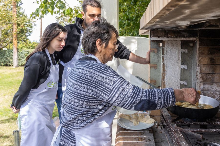 Three people carefully place small stuffed doughs into a wood oven, their hands working in unison, ensuring each morsel finds its place in the fiery embrace of the oven, where they will transform into delectable treats.