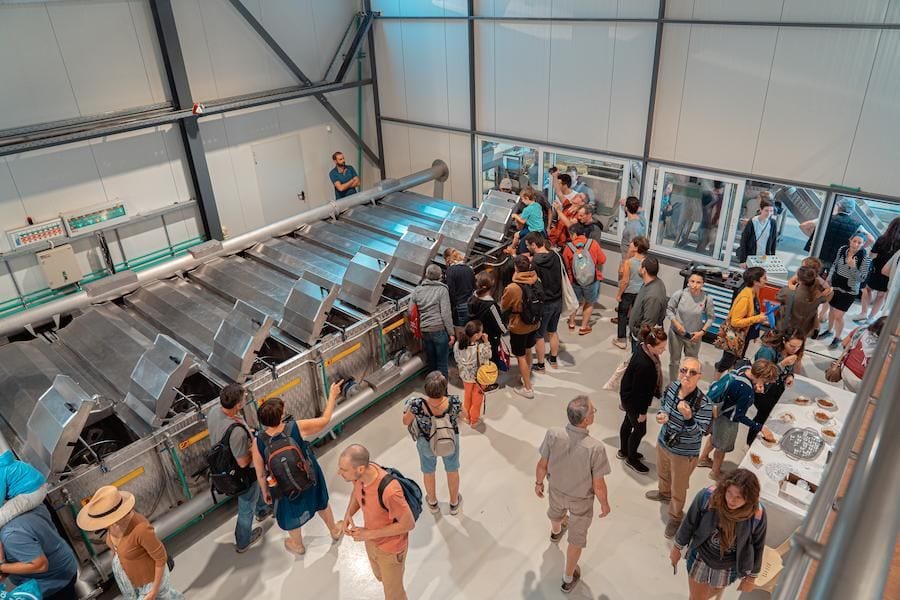 View from above of group of visitors seeing olive oil equipment and machines working at Politakis Olive Oil Mill premises