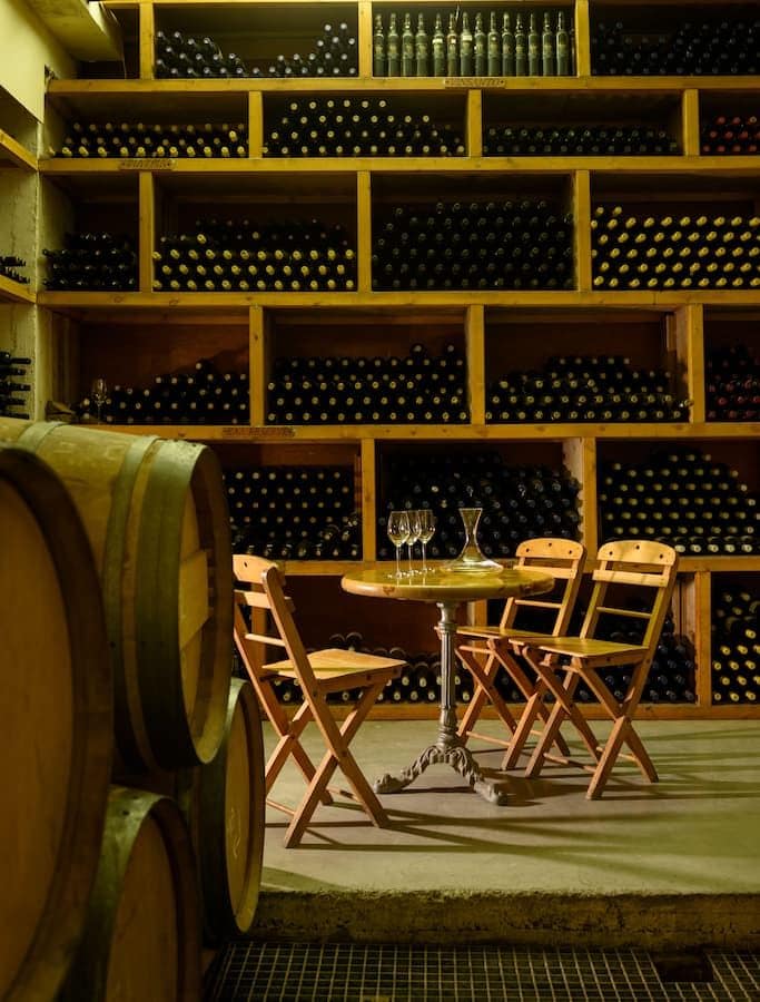 wine wood barrels and table with chairs and stacked wine botles on wooden shelves in the buckground at Boutari Santorini