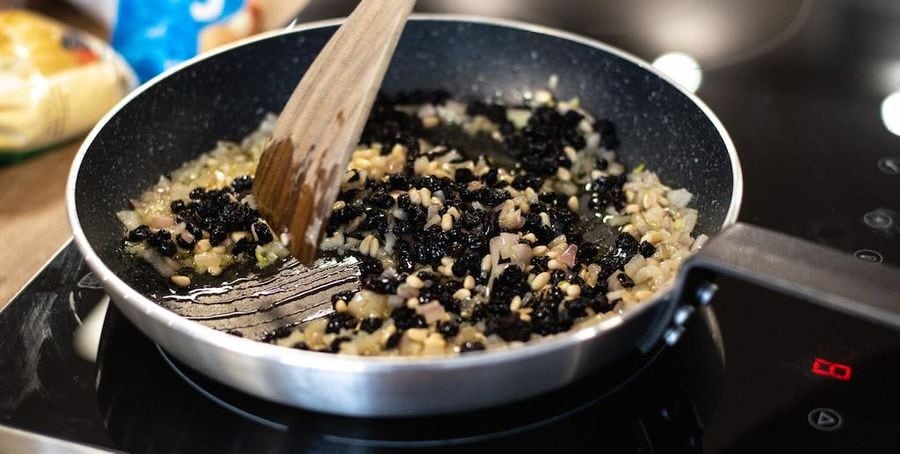 Close-up of a chef cooking chopped onions and black raisins in a pan at Savor Nafplio