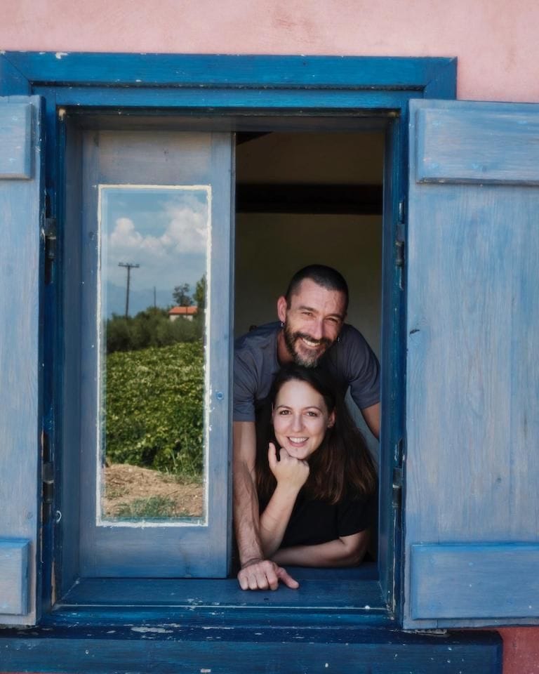 a couple smiles at the camera from a window at Rouvalis Winery