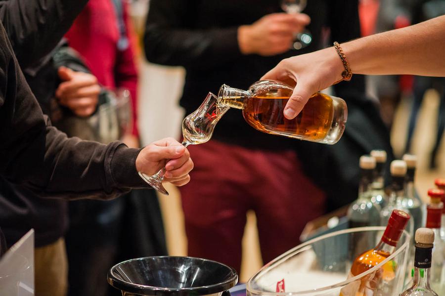 a man holds a glass and a woman pours him a drink from a bottle||