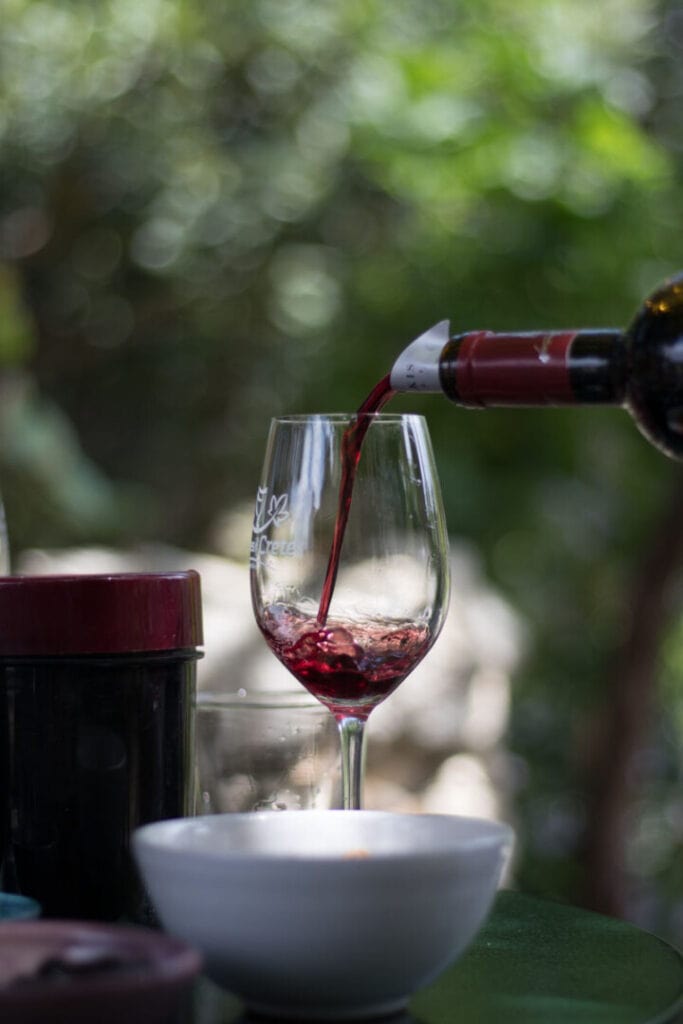 A wine glass sits poised on a table, while a hand gently pours rich red wine into it. The mesmerizing moment captures the anticipation of indulging in the velvety pleasures of a fine vintage.