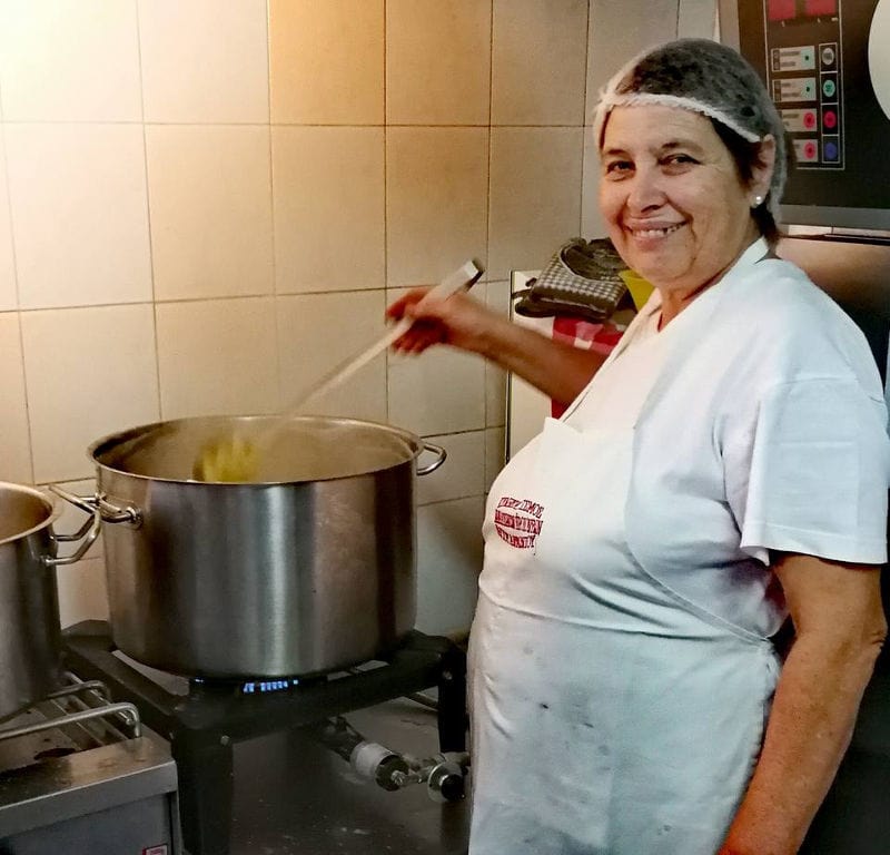 woman mixing with a ladle in a cauldron and smiling happily at the camera at 'Agios Antonios Women’s Agri Cooperative'