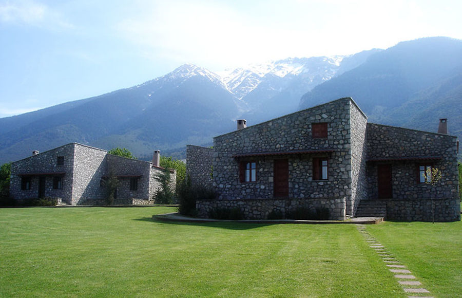 complex of Amfikaia stone buildings surrounded by green lawn and mountains with snow on the background