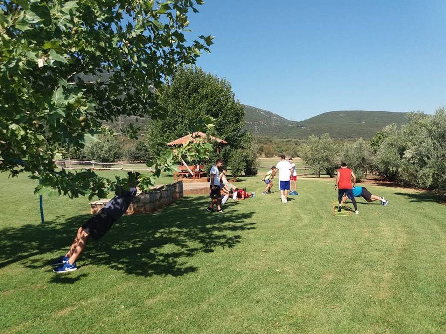 tourists playing football on the green grass surronded by Amfikaia trees