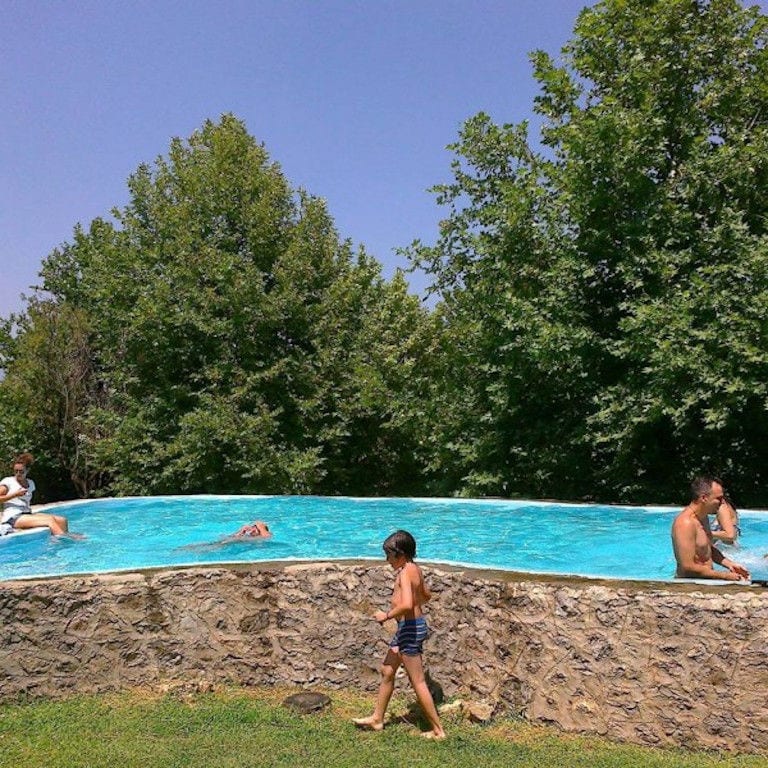 tourists swimming in the Amfikaia stone piscine with trees on the background