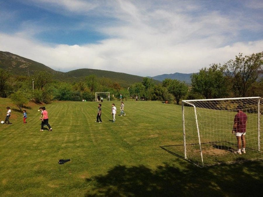 tourists playing football on the Amfikaia soccer field with trees on the background