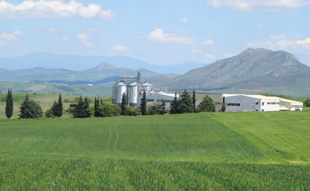 far view of Antonopoulos Farm plant surrounded by green crops and mountains in the background|