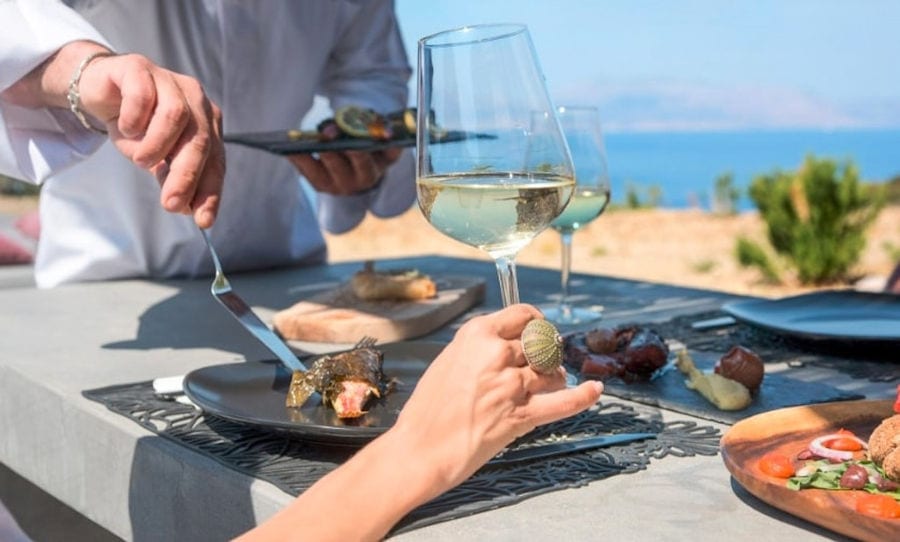 woman holding a glass of red wine and chef served cooked octopus with carrots and sauce from 'Astarti'