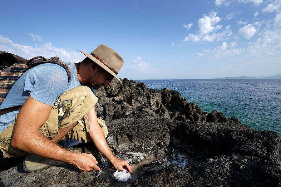 man with a hat collecting salt from the rocks at the sea coast in 'Astarti' area
