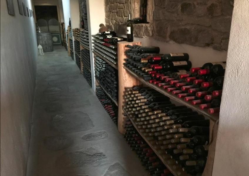 a corridor of the cellar, full of wine bottles on wooden shelves under stone wall at Afianes wines