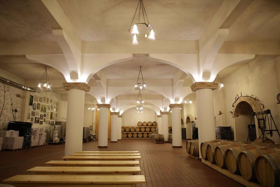 illuminated Tzivani Bio Wines cellar with chandelier hanging from the ceiling with marble columns and wooden barrels on the one side