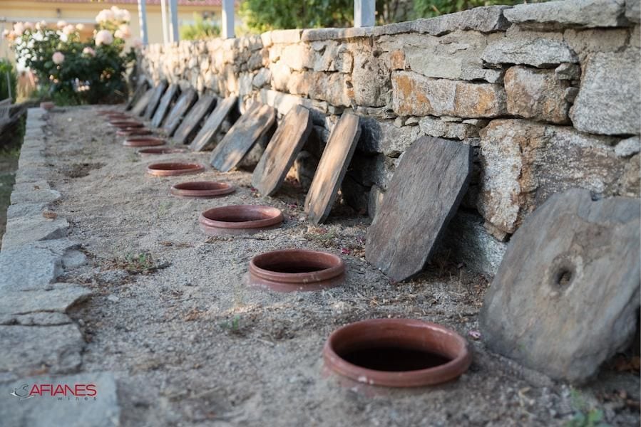 ceramic pots in line, half-burried in the sand outside at Afianes wines and the wooden covers supported by stone fence