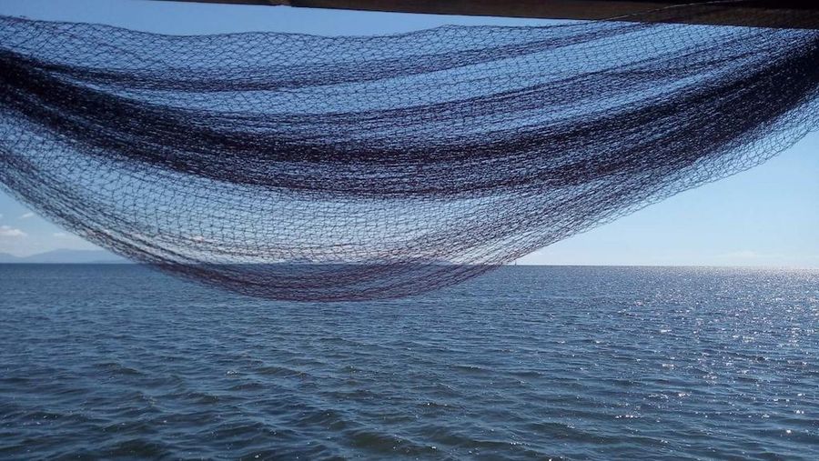 close-up of fishnet hanging above the ground and the sea in the background from Stefanos Kaneletis