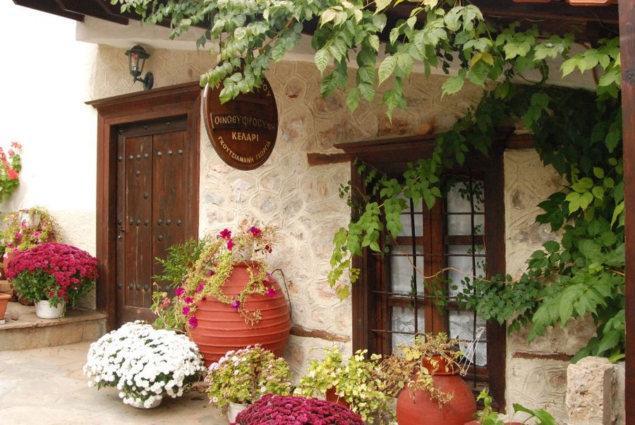 'Dio Fili' winery entrance with wood doors and ceramic pots with flowers on the both sides