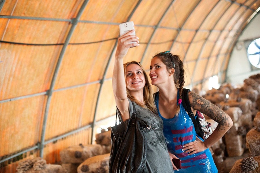 two girls smiling happily and taking selfie photo in 'Dirfis Mushrooms' greenhouse