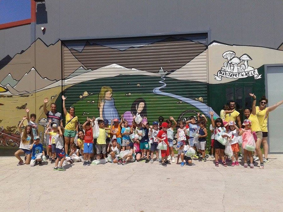 a group of children says hello to the camera with 'Dirfis Mushrooms' wall painted in the background