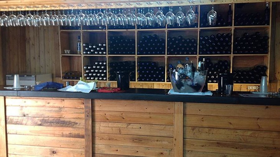 wood bar at 'Domaine Anagennisi' in the background of wine bottles in the storage locker