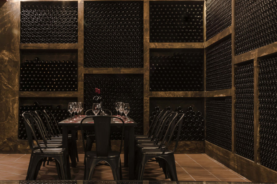 bottles in the storage locker and a wood table with chairs and glasses at 'Domaine Bairaktaris' cellar