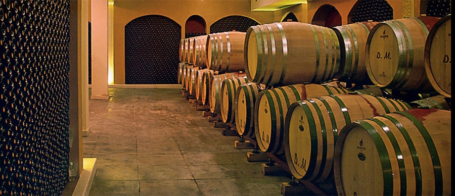 wine barrels on top of each other and stacked bottles on the wall at 'Domaine Migas' cellar