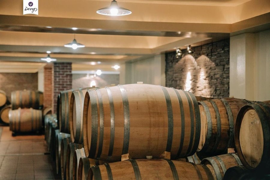 lying wooden barrels in a row on top of each other at 'Dougos Winery' cellar with stone columns