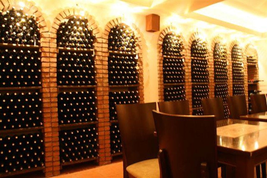 'Dougos Winery' cellar with wine bottles on top of each other storaged in the stone wall and a wood table