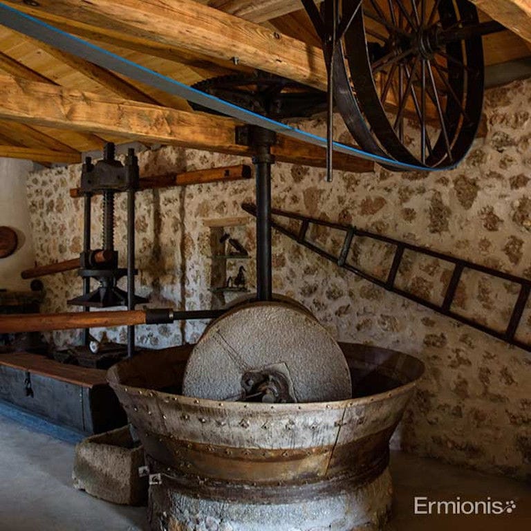 traditional olive press in front of stone wall at 'Olive Oil Museum, Ermionis Bairaktaris Apiary' and and other equipment in the background
