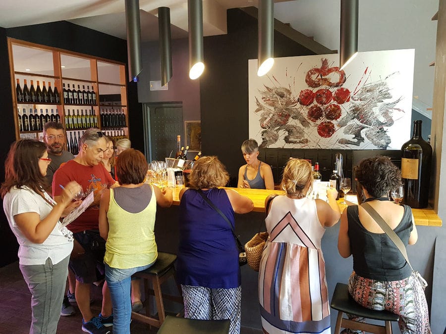 tourists sitting at Constantin Gofas Estate illuminated reception tasting room with a painting in the buckround