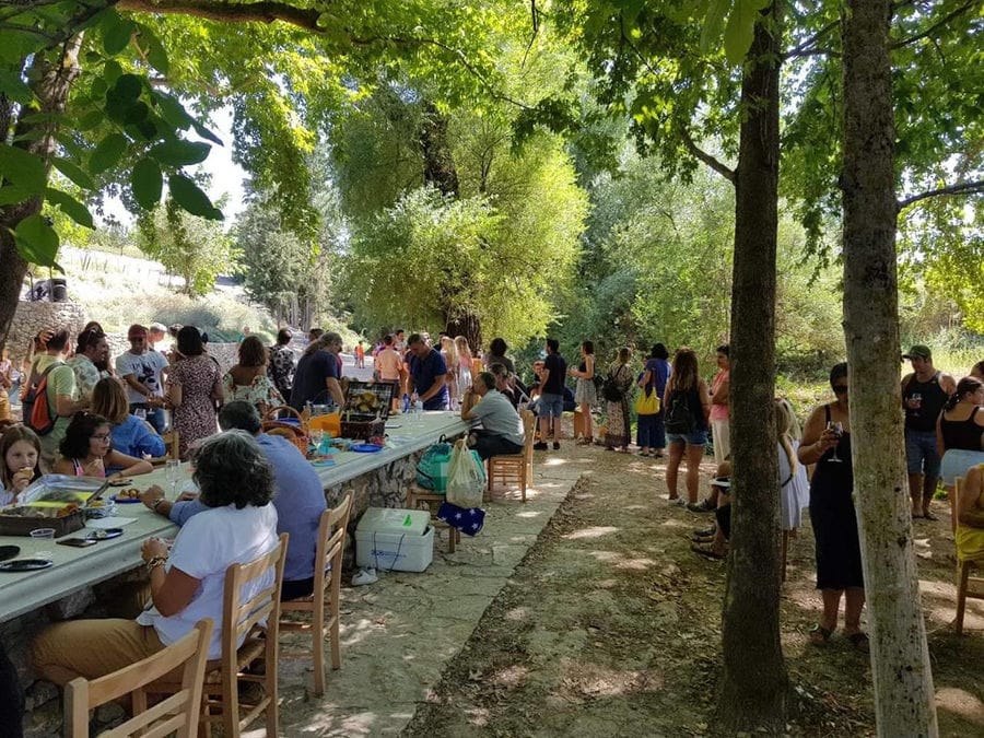 tourists sitting and eating at the tables in the shade of the trees at Constantin Gofas Estate outside