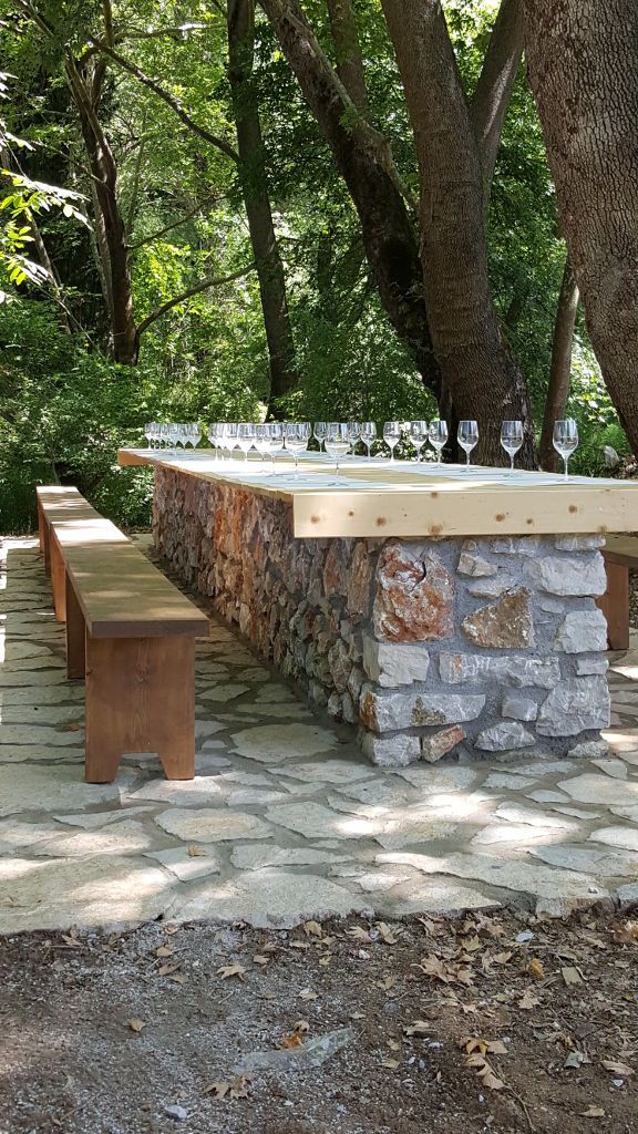 stone table with benches and glasses of wine in the shade of the trees of Constantin Gofas Estate garden