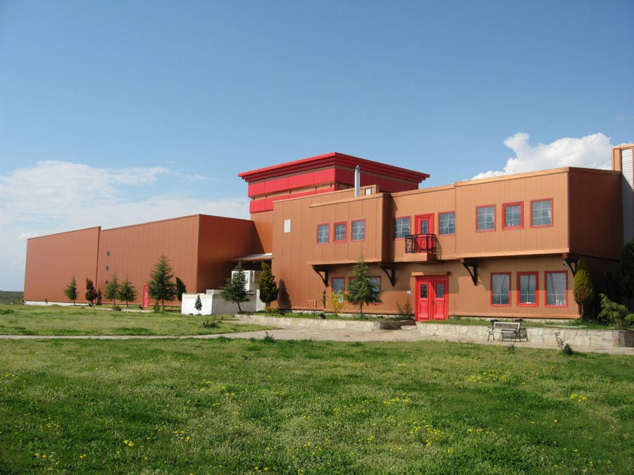 'Evritika Kellaria' building with brown walls and red windows and green lawn in front it