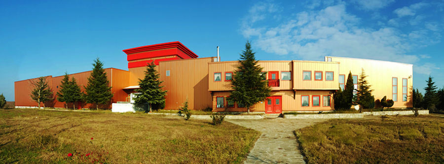 'Evritika Kellaria' building with brown walls and red windows and green lawn in front it