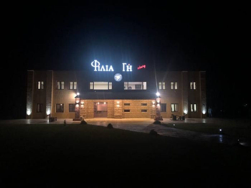 front view of illuminated 'Filia Gi' building by night with green lawn and stone alley