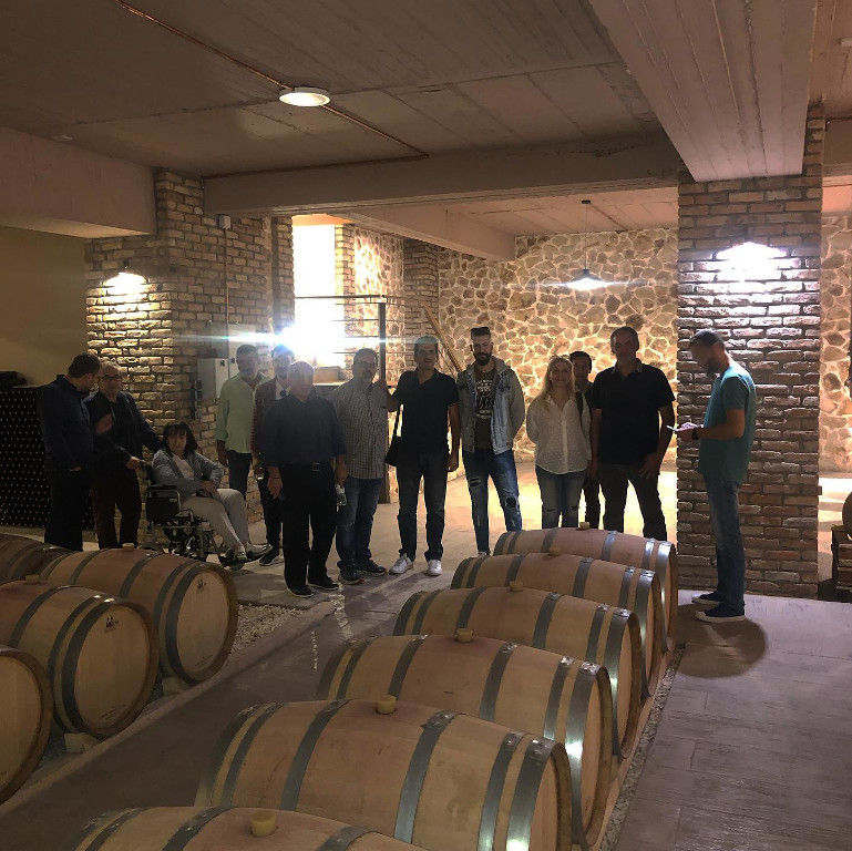 tourists listening to a guide at illuminated 'Filia Gi' stone cellar with wood barrels