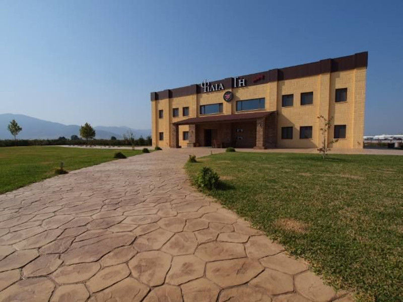 front view of 'Filia Gi' building with green lawn and stone alley and trees and mountains in the background