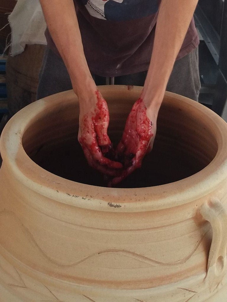 man mixing with his hands in a ceramic amphora, the must 'pulp' of black grapes at 'Domaine Foivos' facilities