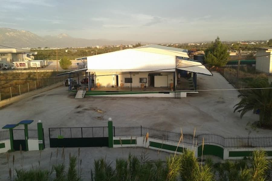 front view of industrial Feréikos building surrounded by pavement, trees and low metal fence