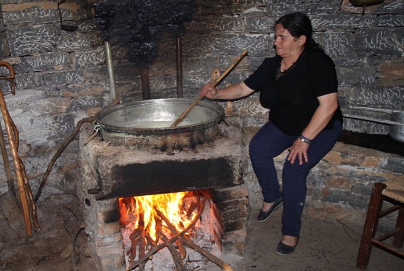 an old woman mixes in a cauldron the food that is cooked on fire wood|close-up of plate with pieces of Greek bobota|close-up of bowl with Greek petimezi and a spoon sweet on the top|close-up of two pieces of Greek zaxaropsomo with surar on the top|aluminum pan with cooked Greek tsigarides|close-up of plate with cooked Greek trahana and a spoon on the top|close-up of two pieces of Greek revithopsomo