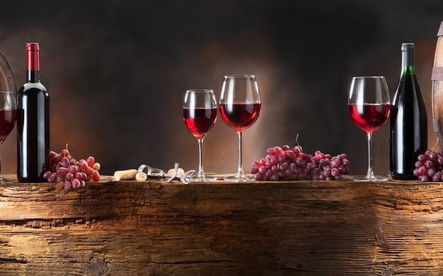 glasses with red wine and grapes and bottles on the table