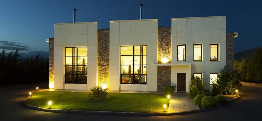 illuminated 'Katsaros Distillery' building by night with pavement and green lawn in the front
