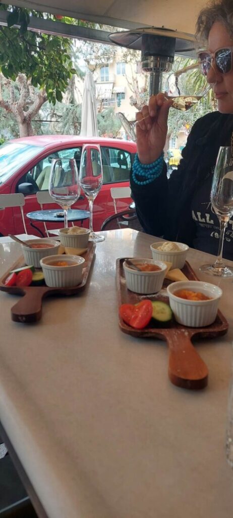 A lady examines a glass of white wine while enjoying an assortment of delicacies on a plate in front of her.