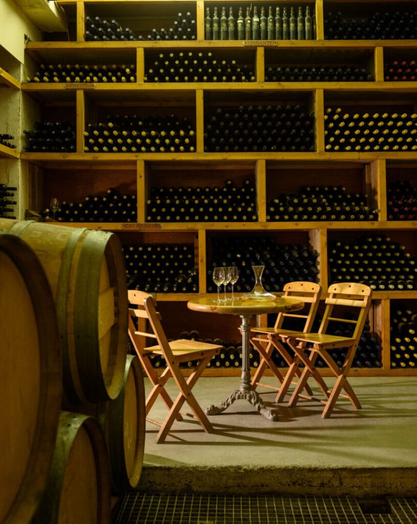 wine wood barrels and table with chairs and stacked wine botles on wooden shelves in the buckground at Boutari Santorini winery original