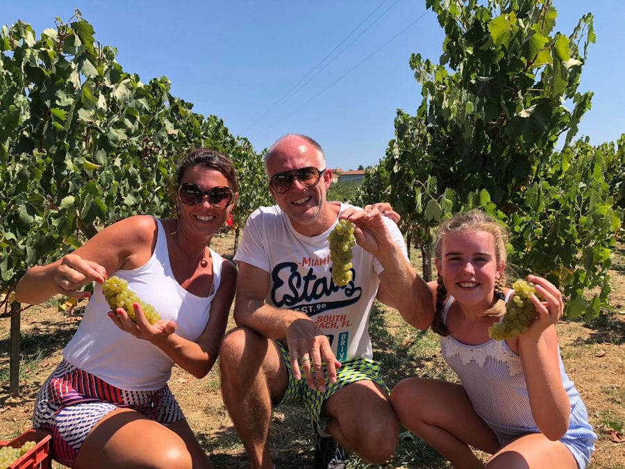 a couple with a little girl smiling happily at the camera and keeping bunches of grapes in their hands in Klima Grampsa vineyards
