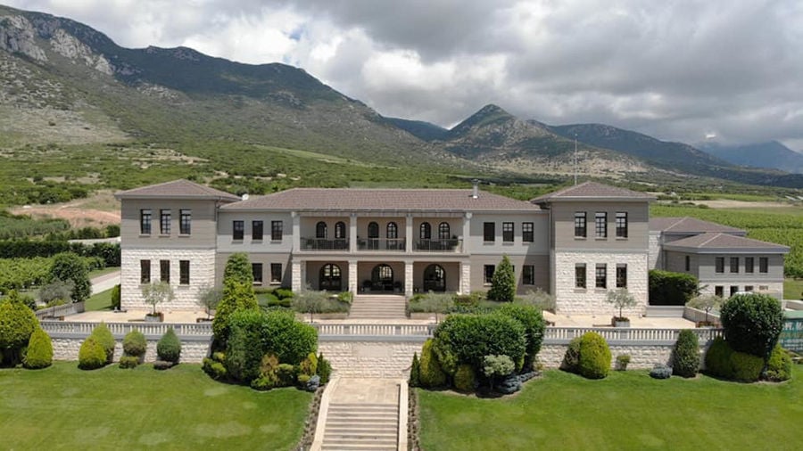 front view of 'Ktima Biblia Chora' with steps stairs and plants and green lawn on the both sides and mountains in the background