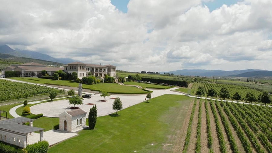 far view of 'Ktima Biblia Chora' surrounded by plants and green lawn and vineyards and mountains in the background