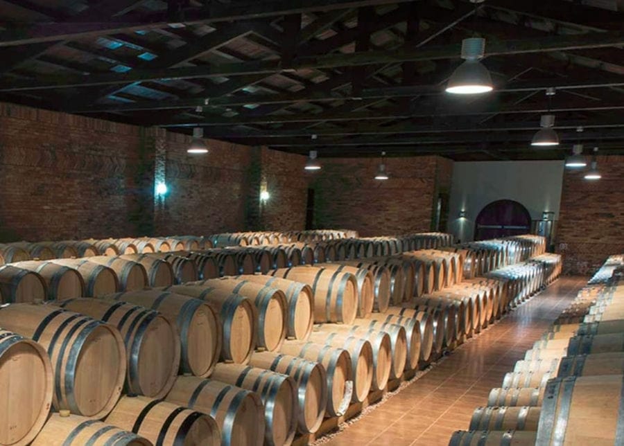 wine wood barrels on top of each other in a row at illuminated 'Ktima Biblia Chora' cellar