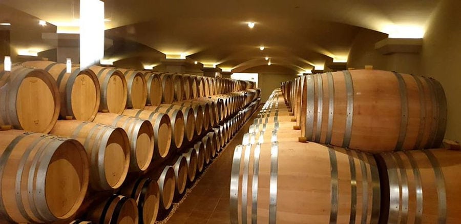 wine wood barrels on top of each other in a row at illuminated 'Ktima Biblia Chora' cellar