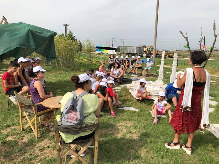 a group of pupils listening to a woman giving a tour at Efkarpia Farm outside