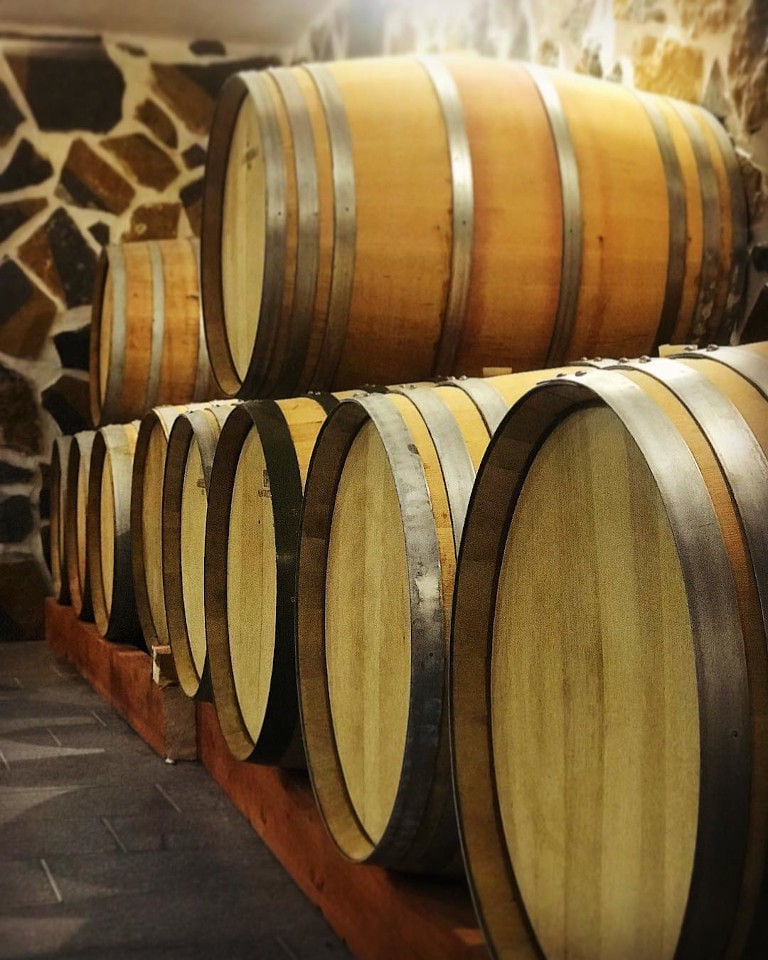 lying wine barrels on top of each other on wood selfs at Ktima Karamitsos stone cellar